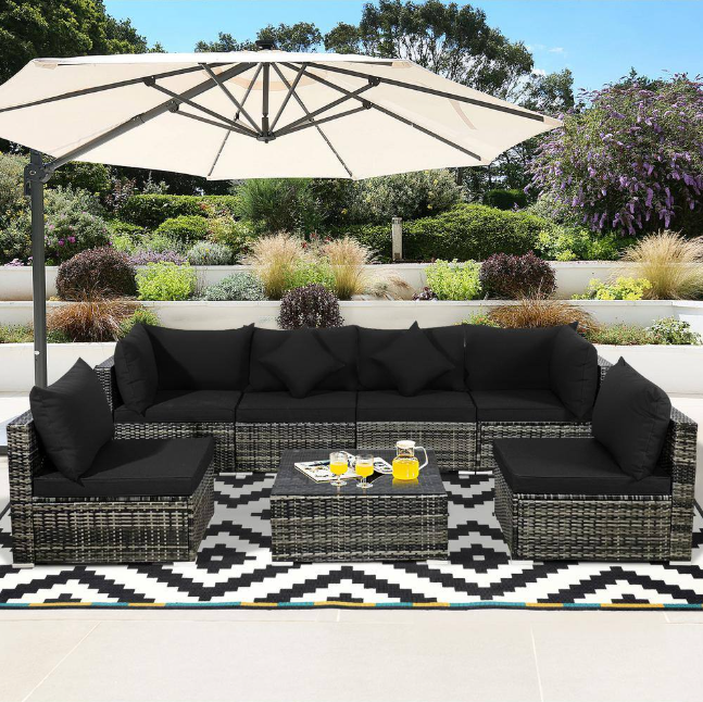 Outdoor wicker patio furniture set with black cushions arranged on a deck