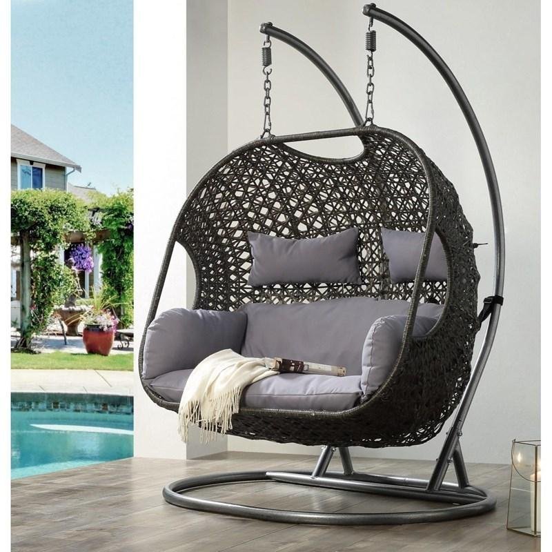 Wicker porch swing chair hanging from a black metal stand on a patio.